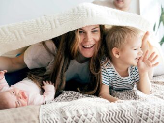 Happy mommy plays with the children on the bed and covers the children and herself with a blanket.